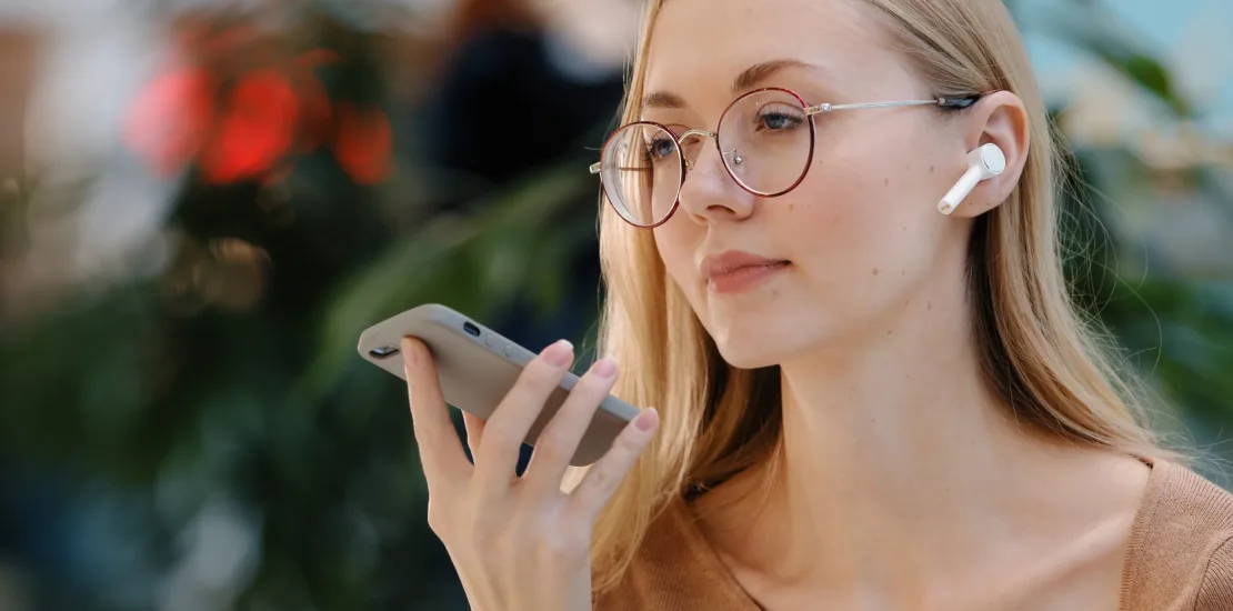 Close up emotional girl use virtual assistant speak in microphone of phone caucasian young lady with glasses talk on speakerphone record audio message using wireless headphones telephone communication. High quality photo