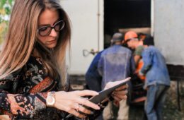 Mobiles Arbeiten - Frau steht mit Tablet vor Umzugswagen und telefoniert nebenbei.