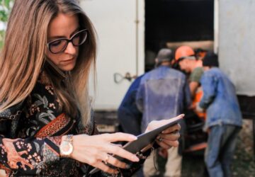 Mobiles Arbeiten - Frau steht mit Tablet vor Umzugswagen und telefoniert nebenbei.